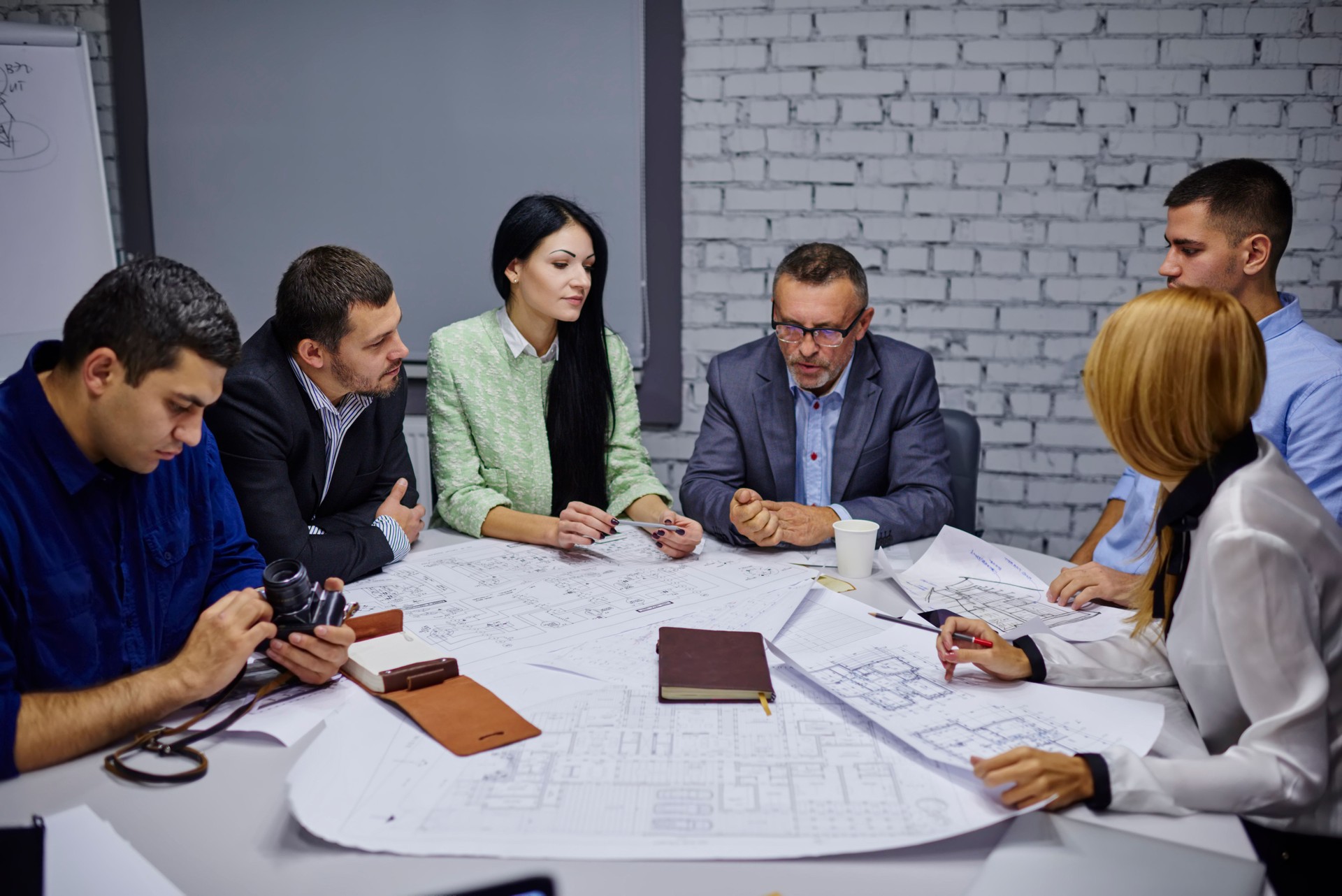 Experienced team of female and male advertise magazine workers together with director of company solving working problems sitting at meeting table with sketches during briefing